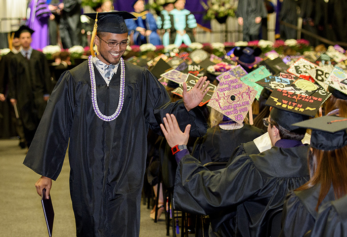 Graduate high fives another student holding his degree.